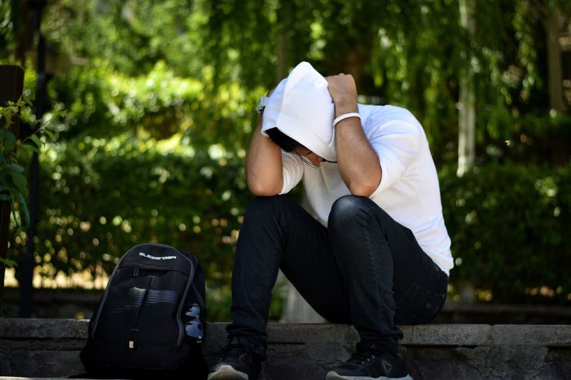 Hombre joven sentado sobre el borde de la acera con las manos sobre la cabeza